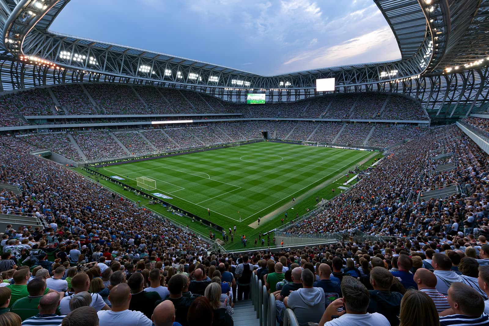 Un grand stade de football rempli de supporters sous les projecteurs, par une soirée d'été.