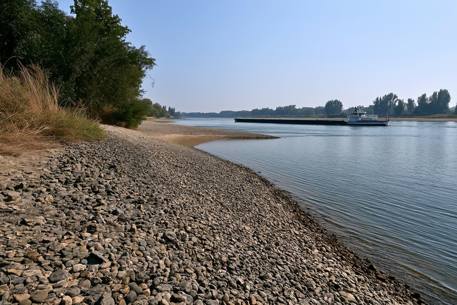 Une barge de charge, basse et légèrement chargée, sur un Rhin rétréci, aux bancs de sable à découvert.