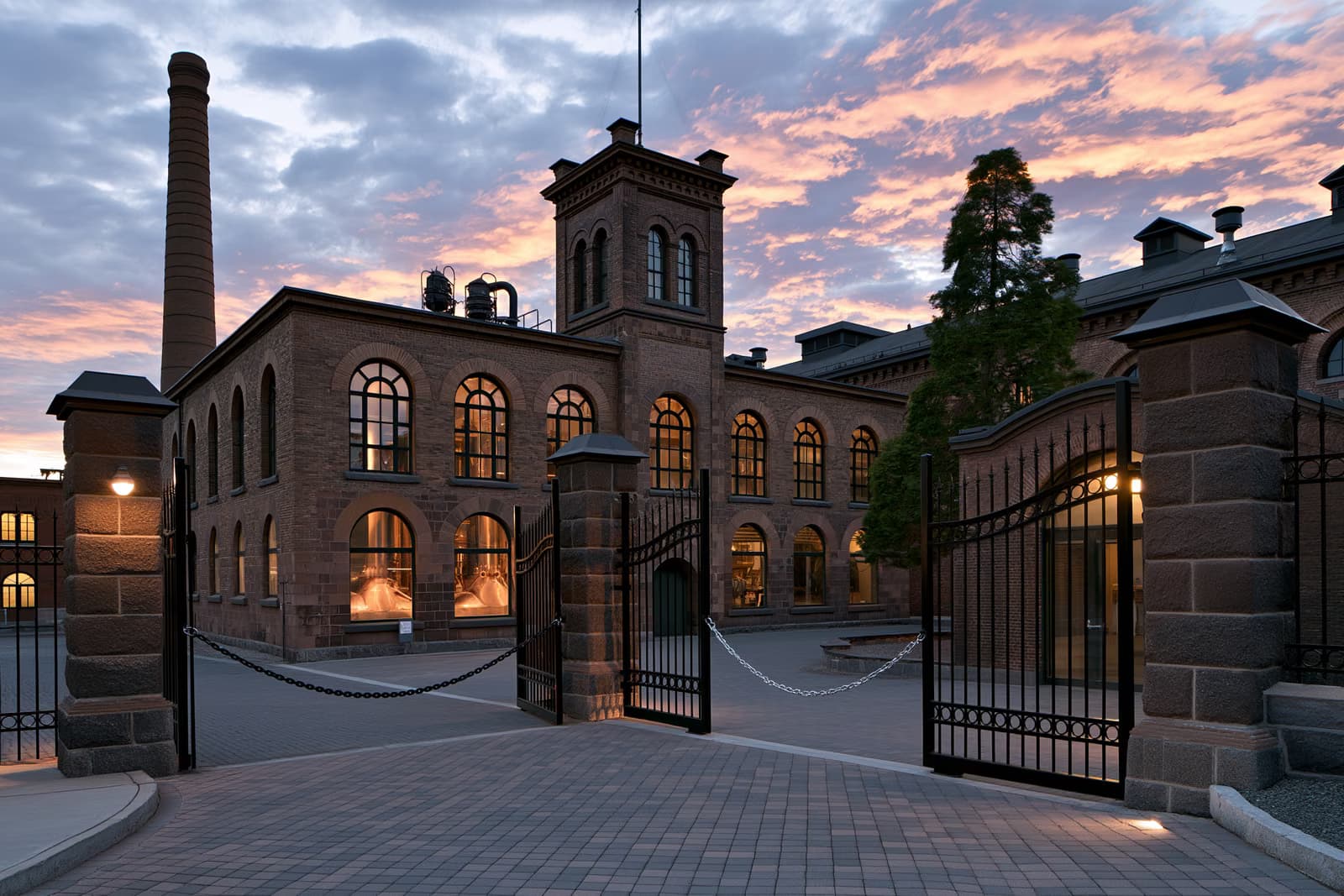 Au coucher du soleil, derrière des grilles enchaînées se dresse un bâtiment historique de brasserie, avec des cuves en cuivre visibles à travers des fenêtres cintrées, marquant la fin de la brasserie Eichbaum.