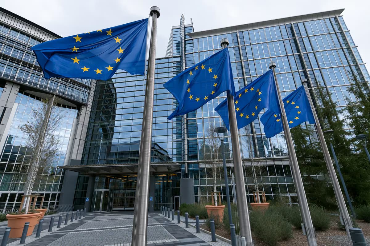 Drapeaux de l'Union européenne flottant sur des mâts devant un bâtiment moderne en verre.